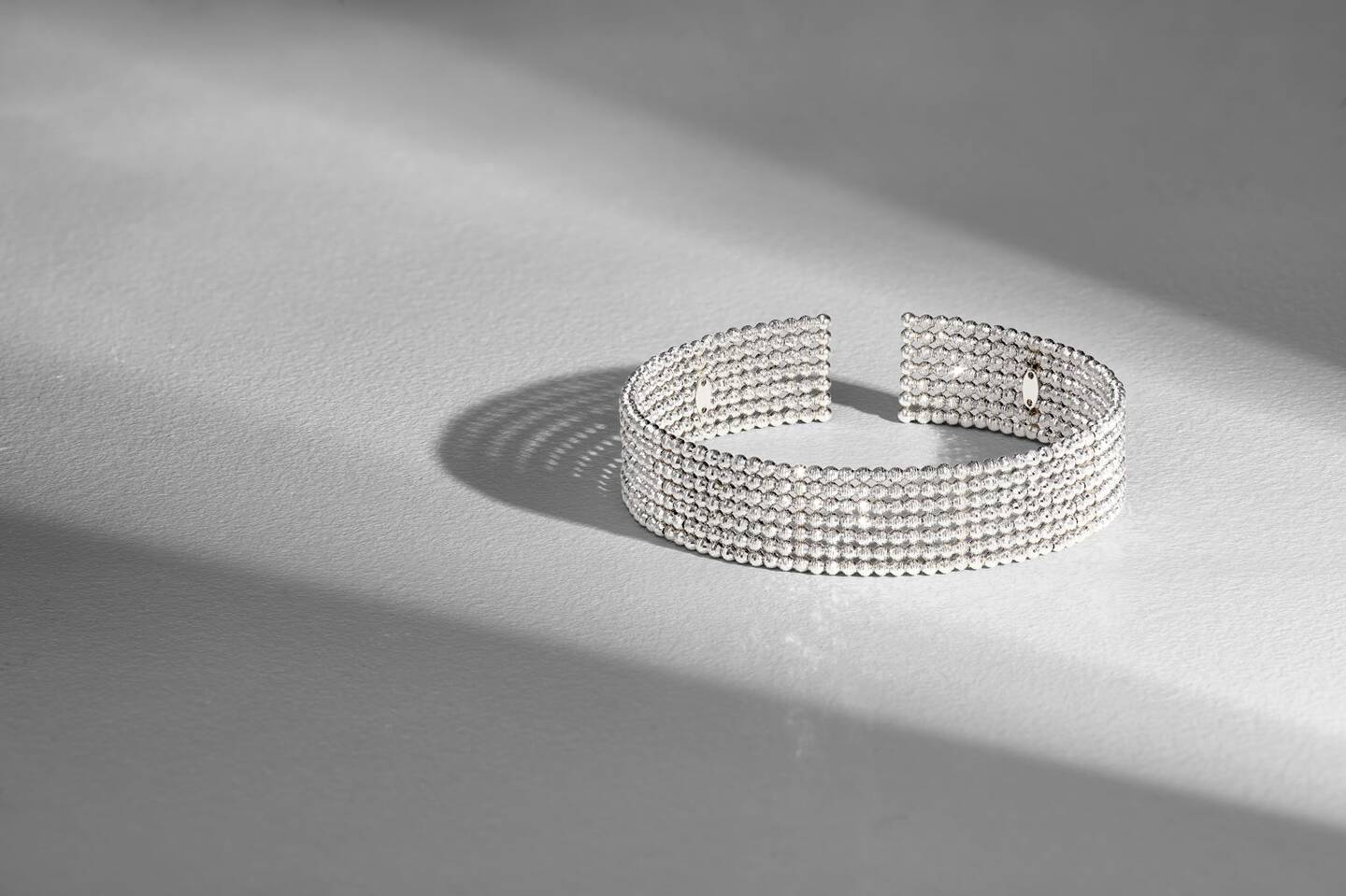 A platinum bracelet on a gray background between two shadows